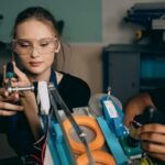 A young woman with safety glasses assembling a robotic device indoors.